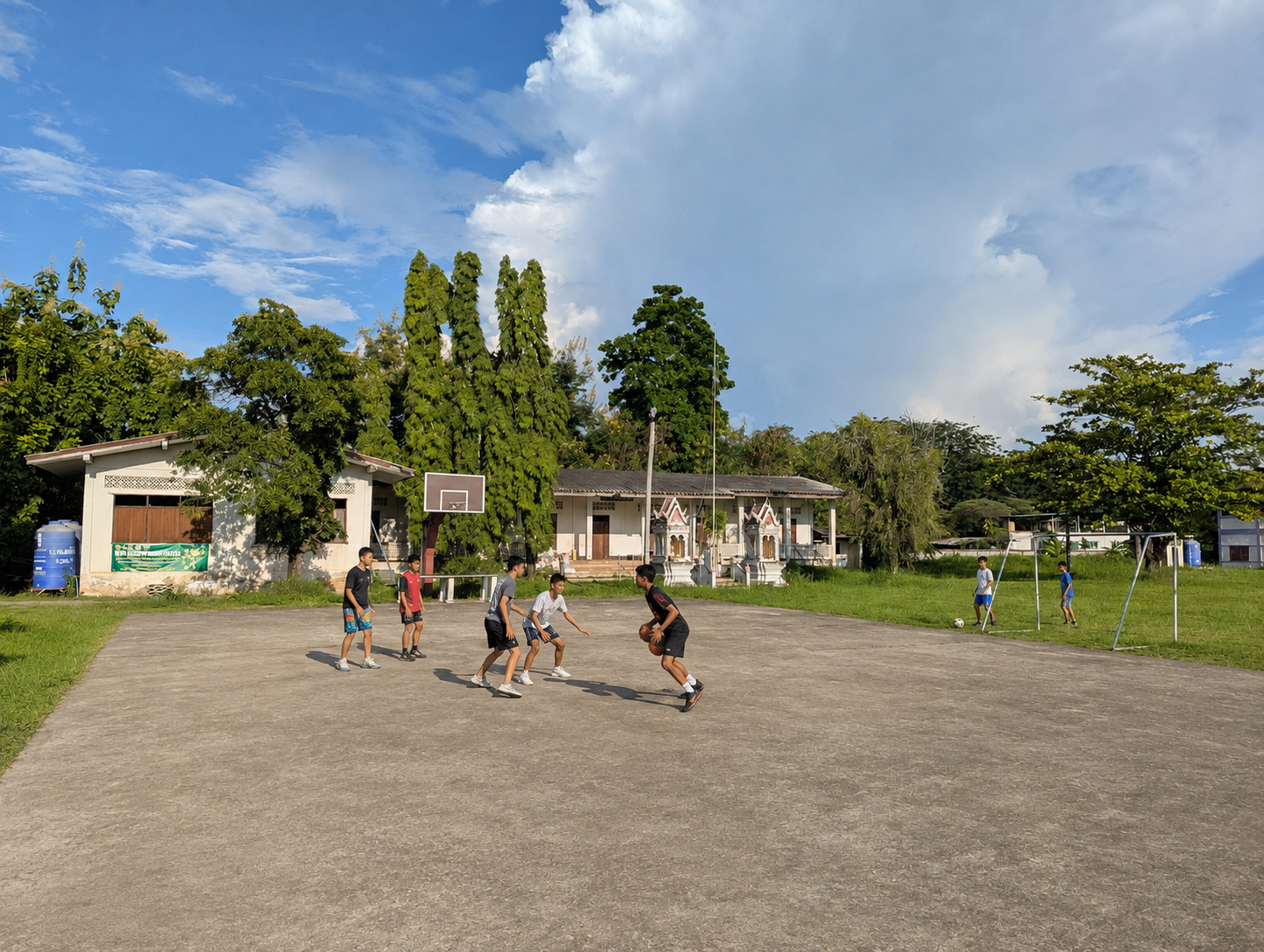 Learners playing basketball on the neighboring outdoor court, with the football field beside them